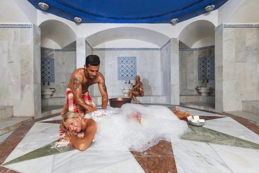 A person lying on a white bath mat in a room with marble walls and blue patterned tiles. 2