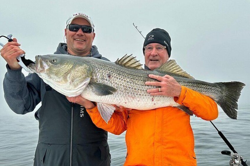 Deux personnes tenant un gros poisson, avec une canne à pêche en arrière-plan. 3