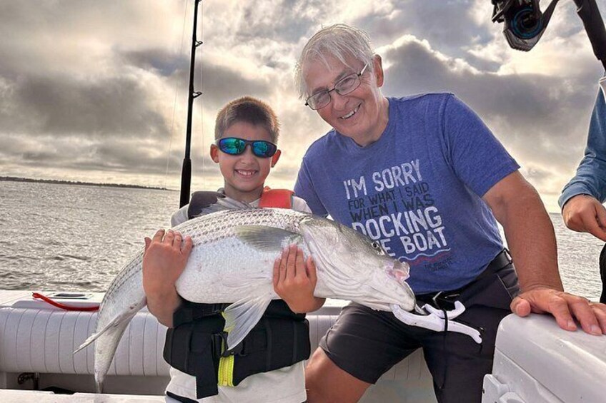 Une personne tenant un gros poisson sur un bateau, avec un ciel nuageux en arrière-plan. 5