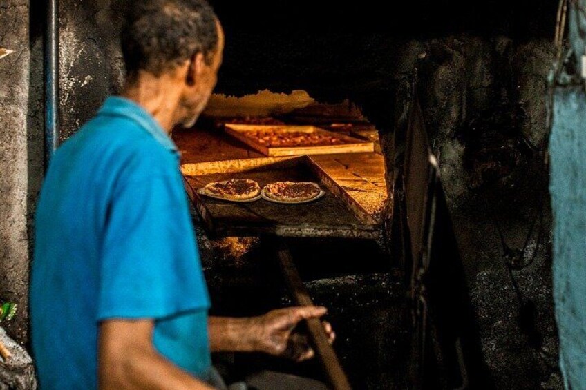 A person in a blue shirt operating a wood-fired oven with pizza. 1