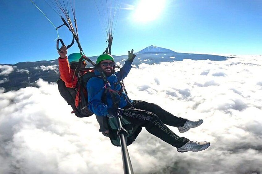 Dos personas practicando parapente sobre las nubes, con una montaña al fondo. 1