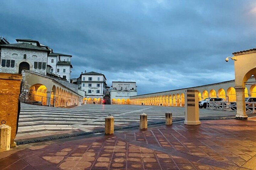 A historic square with a tiled pavement, a bridge, and buildings with illuminated arches. 4