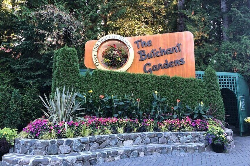 A sign for The Butchart Gardens with a circular window and a stone staircase leading up to it. 2