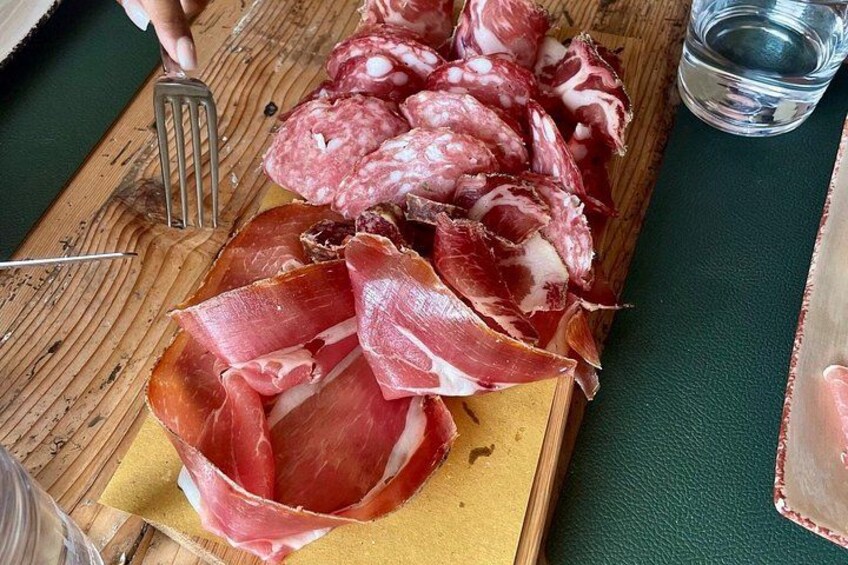 A wooden cutting board with sliced cured meats, a knife, and a glass of water. 3