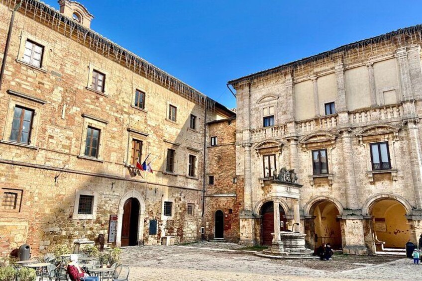 A historic courtyard with stone buildings, arched doorways, and outdoor seating. 1