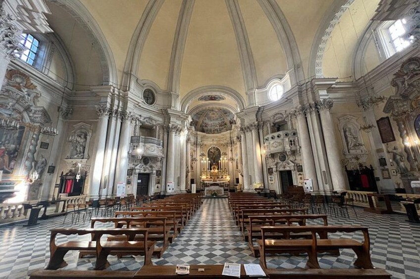An ornate church interior with rows of wooden pews, a checkered floor, and a central altar. 5
