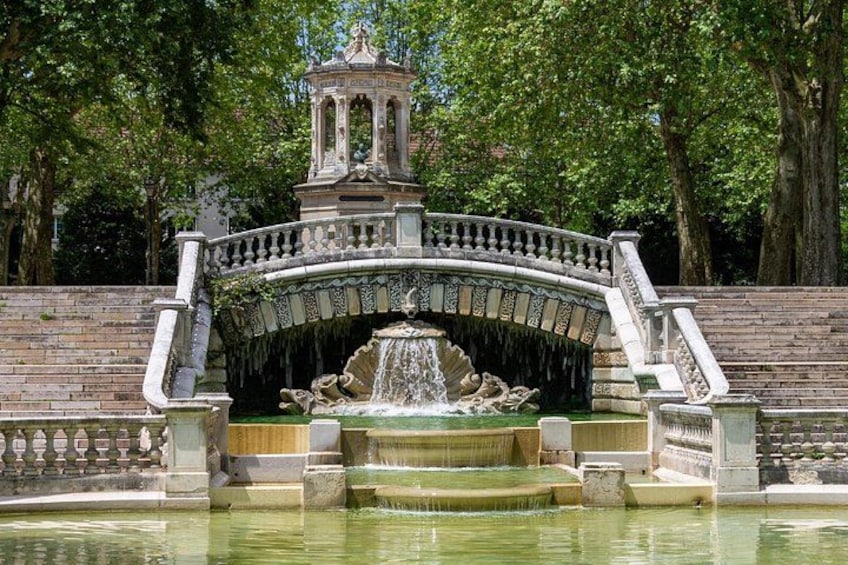 A classical fountain with a central statue, surrounded by a stone balustrade and a brick wall. 2