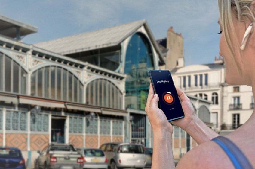 A person holding a smartphone with an app open, standing in front of a building with arched windows and a curved roof. 5