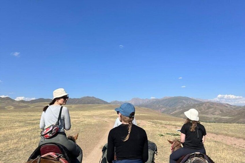 Tres personas montando a caballo por un sendero, con montañas al fondo. 1