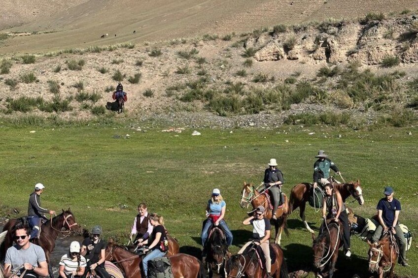 Un grupo de personas montando a caballo por un campo cubierto de hierba, con un paisaje montañoso al fondo. 2