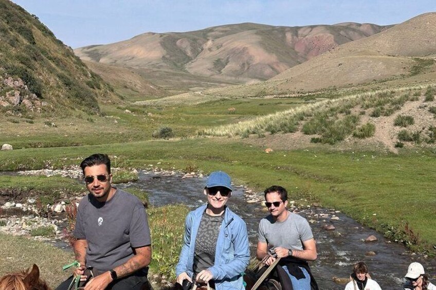 Tres personas sentadas junto a un río en un paisaje montañoso. 4