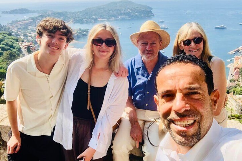 Un grupo de personas está de pie en un acantilado con vistas a un paisaje costero, con edificios y barcos a lo lejos. 2