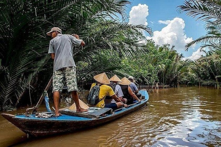 A man standing on a boat in a river surrounded by palm trees. 3