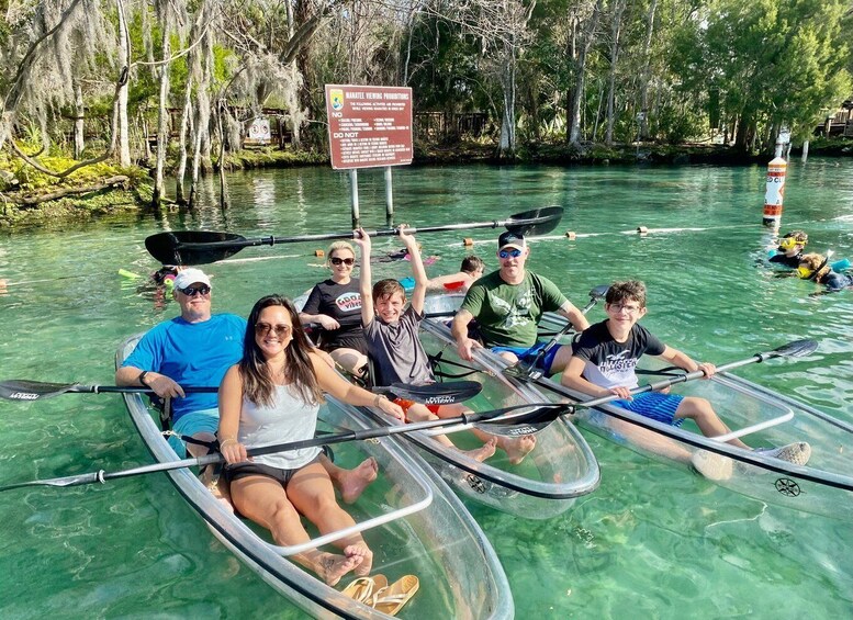 People in canoes on a clear water body surrounded by trees. 1