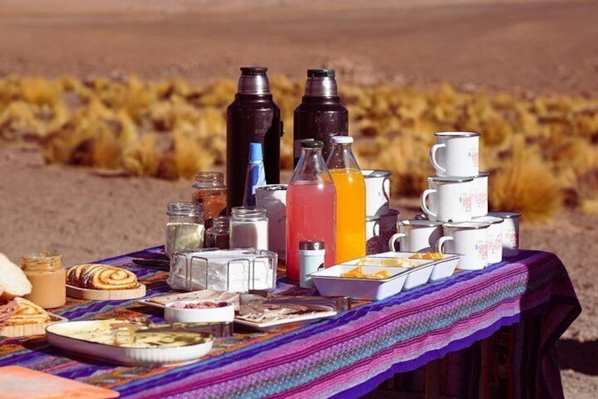 Een picknick met eten, drinken en kampeerspullen op een deken in een woestijnlandschap. 4