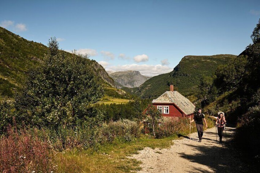 A red house on a dirt path in a mountainous area with hikers. 1
