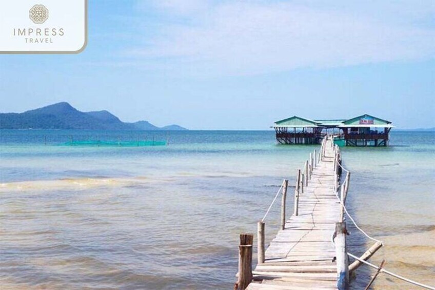 A wooden pier leading to an overwater bungalow with clear turquoise water and distant mountains. 1