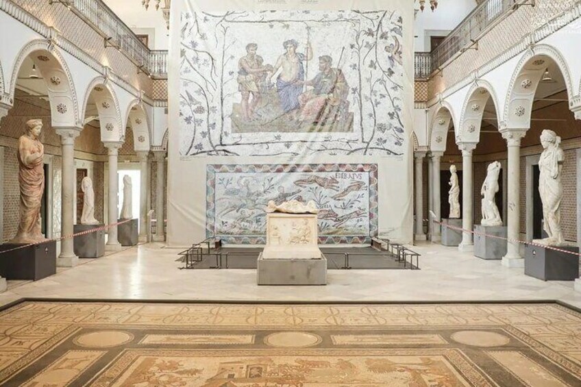 A museum interior with classical statues, a central mosaic, and an arched ceiling. 4