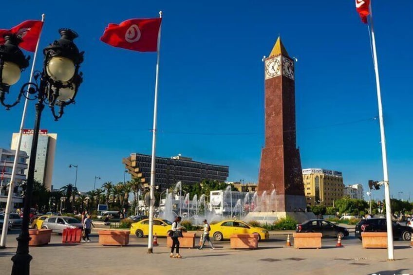 A square with a clock tower, fountains, and red flags. 2