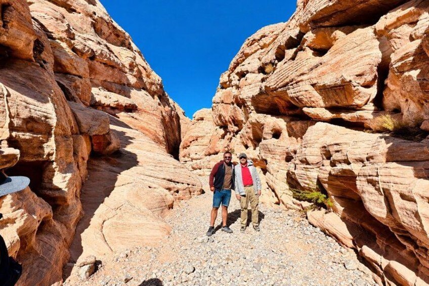 Two people hiking in a rocky canyon with layered rock formations. 1