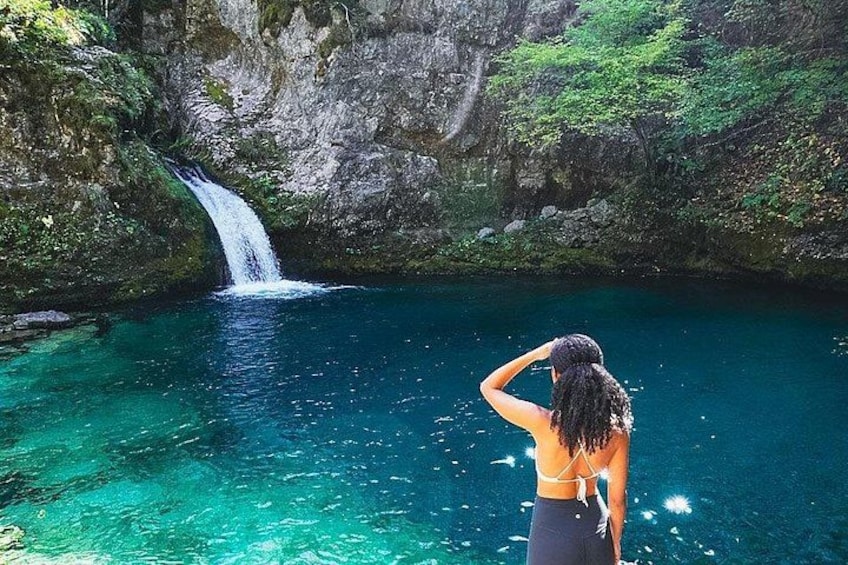 Een waterval, helderblauw water en een persoon die bij het water staat. 2