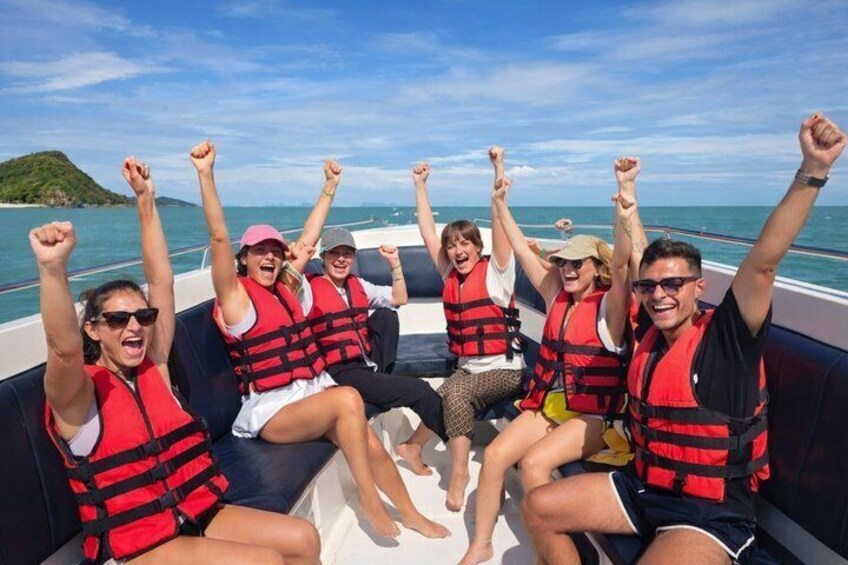 A group of people on a boat wearing life jackets, with the ocean and a small island in the background. 3