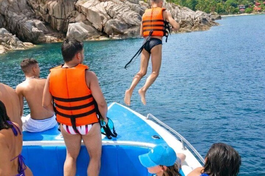 People on a boat, some wearing life jackets, with rocky cliffs in the background. 2