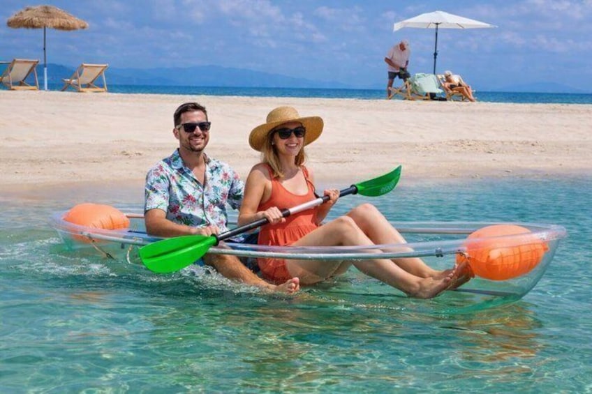 A couple in a kayak on a beach with clear water, sun, and beach umbrellas in the background. 1