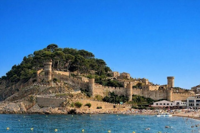 A coastal fortification with towers, a beach, and a clear blue sky. 3
