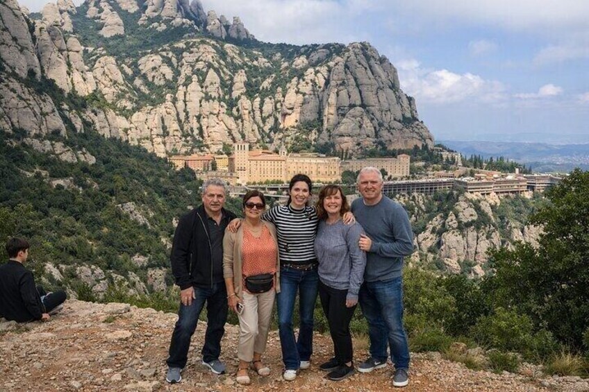 A group of people standing on a rocky outcrop with a mountainous landscape and a building in the background. 4