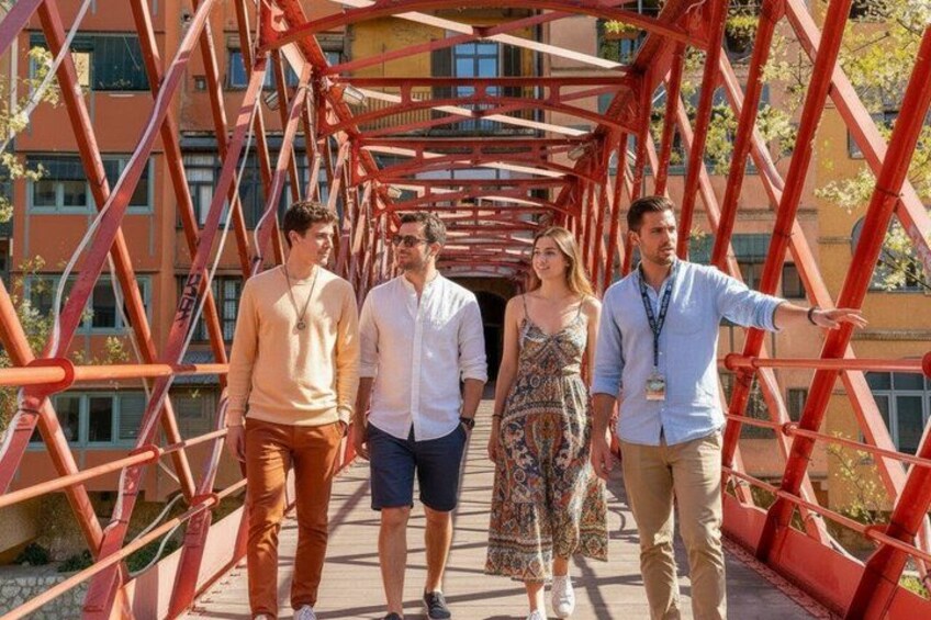 Un grupo de personas caminando sobre un puente de metal rojo con edificios al fondo. 1