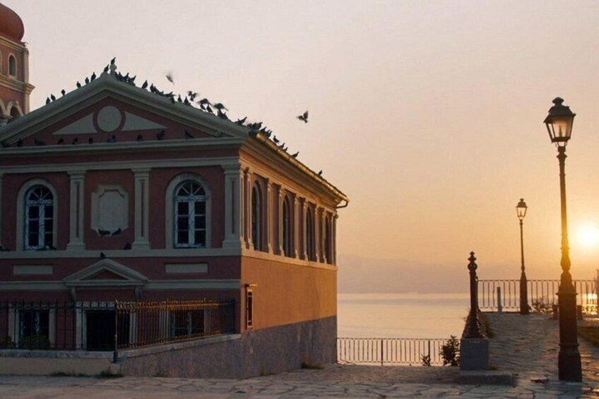 A historic building with a red facade and a dome, a coastal walkway, and a street lamp. 2