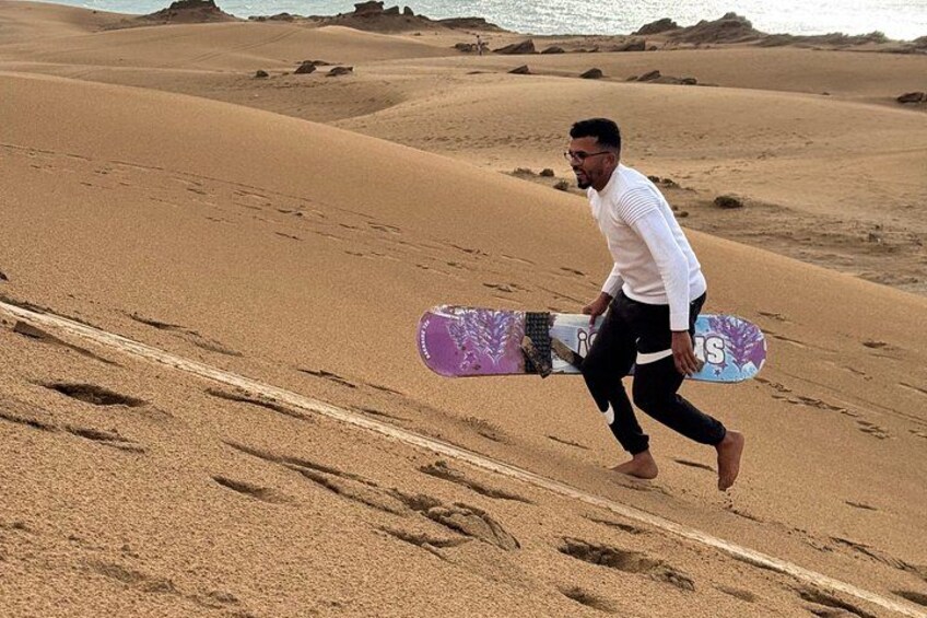 Una persona corriendo en una playa arenosa dejando huellas, llevando una tabla de snowboard. 5