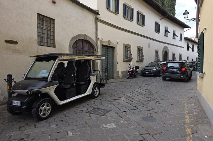 Une rue pavée, avec une voiturette de golf garée à gauche, une moto au milieu et une voiture à droite. 3