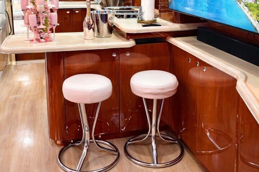A wooden bar area with two pink bar stools and a TV screen. 2