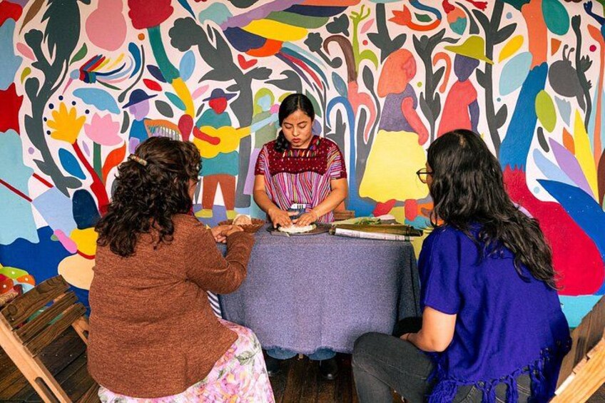Una mujer sirve comida en una mesa con un mural colorido de fondo. 2