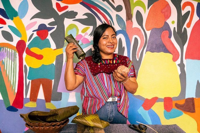 Una persona sostiene una cesta tejida tradicional frente a un mural colorido. 3