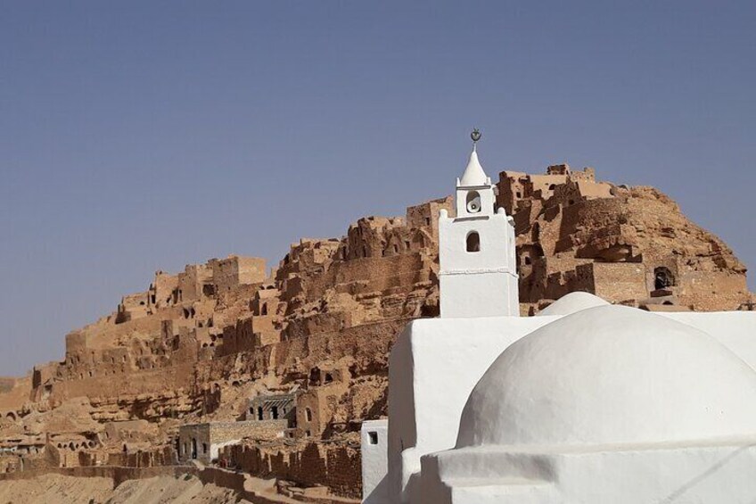 En vit moské med ett minaret på en kulle, omgiven av antika ruiner. 2