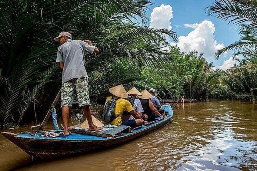 A man standing on a boat in a river surrounded by palm trees. 3