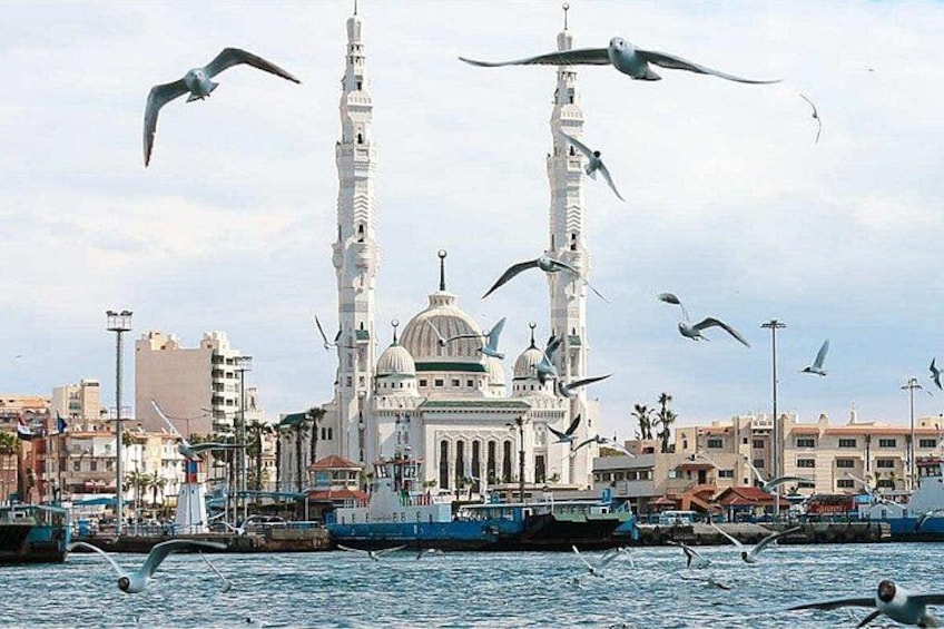 A mosque with two tall minarets, a dome, and a waterfront with boats and seagulls. 1