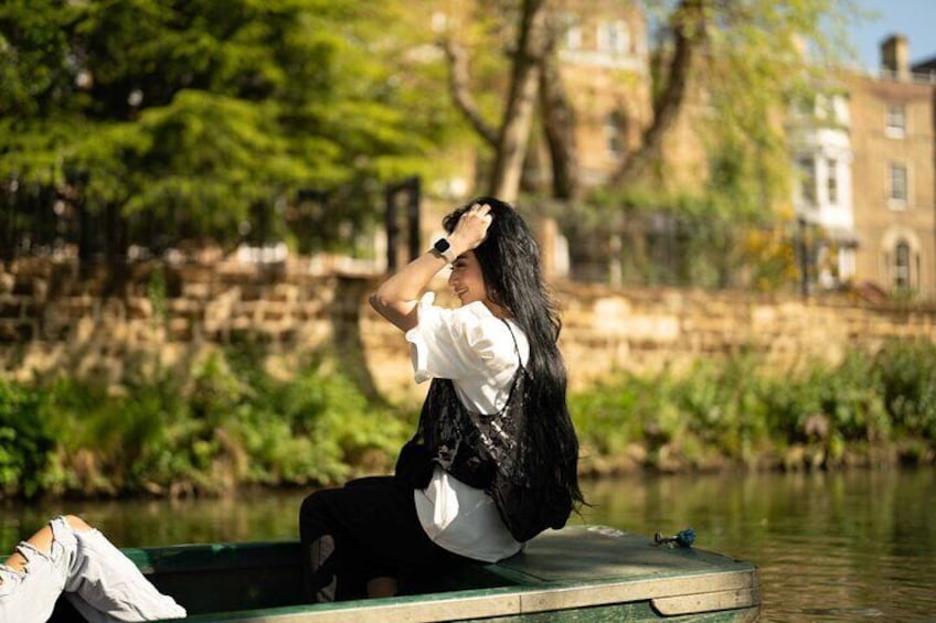 A person sitting on a dock by a river with buildings in the background. 1
