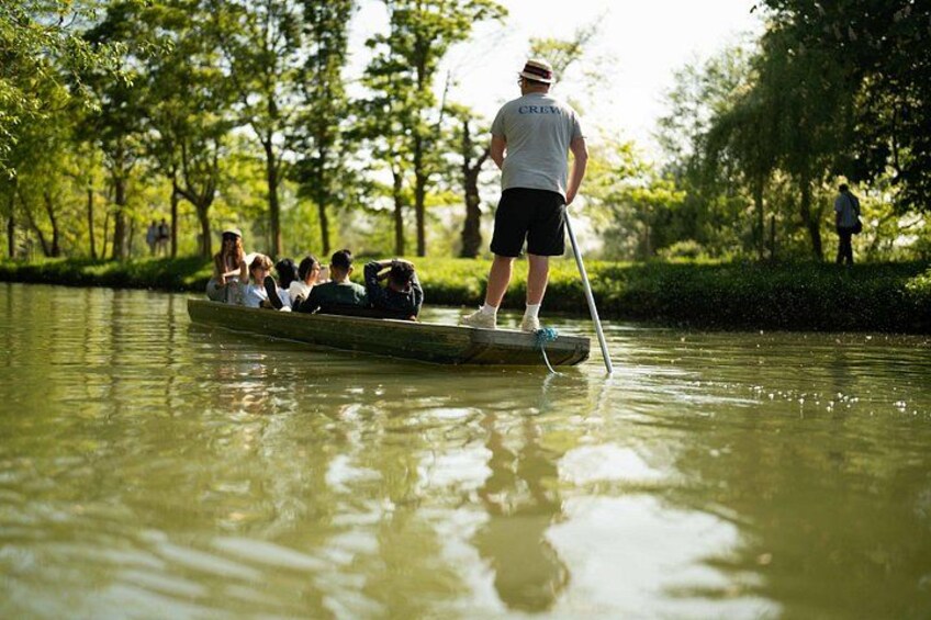 A group of people in a rowboat on a calm river, surrounded by lush greenery. 5
