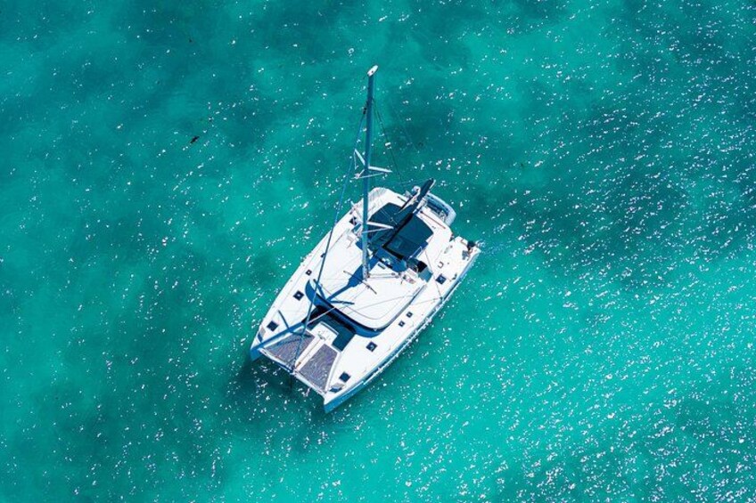 A white boat with a mast and sails on turquoise water. 4