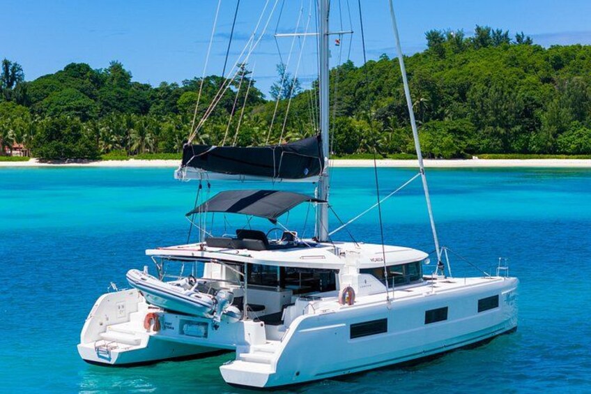 A white catamaran with a black canopy sailing on turquoise waters. 1