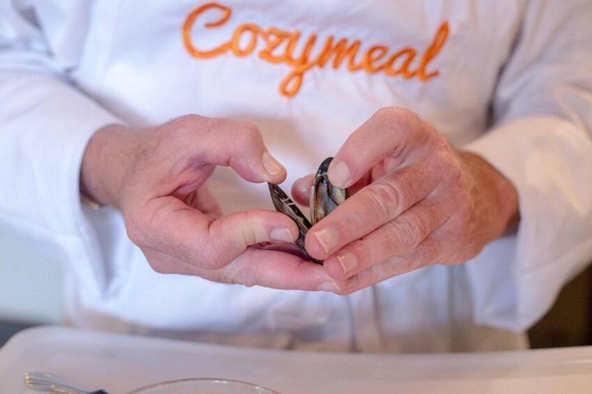 A person wearing a white shirt with 'Cozymeal' written on it, holding a small object. 3