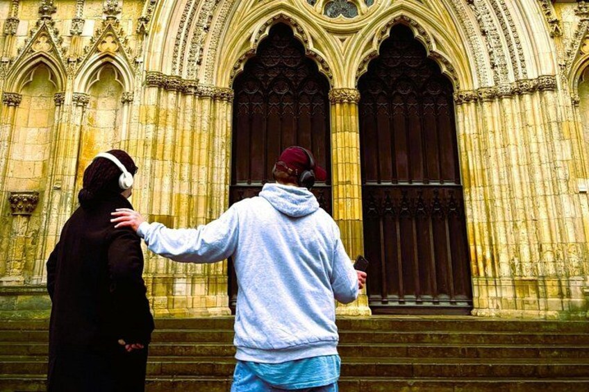 Two people standing in front of a historic building with large wooden doors and intricate stonework. 3