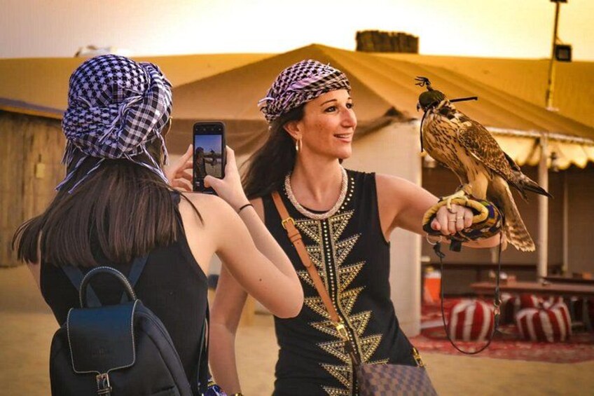 Two people with a falcon, one taking a photo, in a tented area. 3