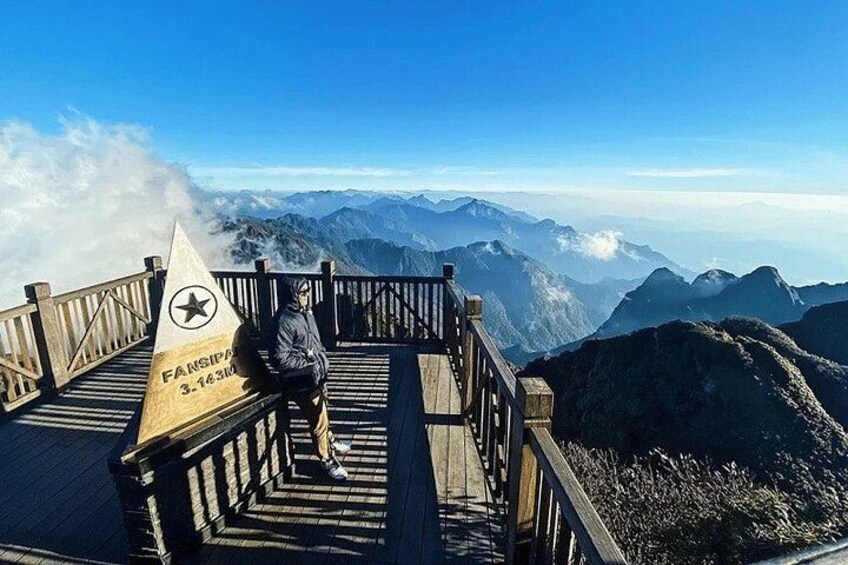A person sitting on a wooden observation deck with a mountain view. 3