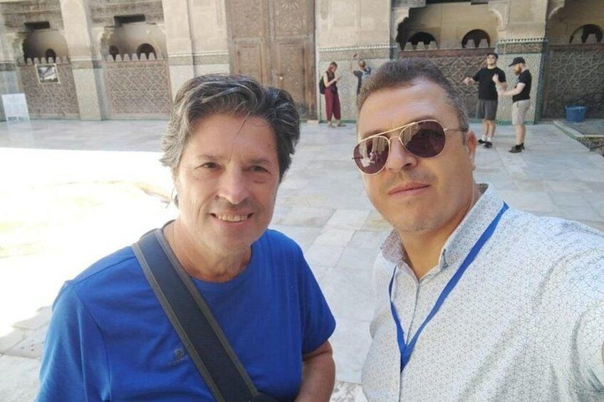 Two individuals in a courtyard with architectural arches and a tiled floor. 2