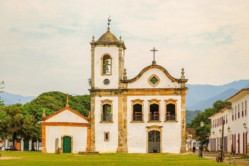 A historic church with a bell tower and a smaller adjacent building, surrounded by a grassy area and other buildings. 1